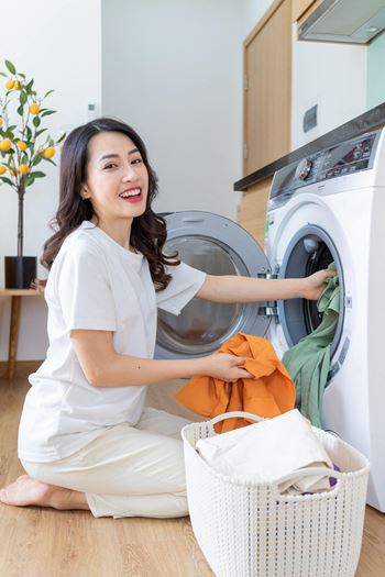 Young Asian woman washing clothes while kneeling on the floor by the dryer. at Canyon Terrace Apartments, California
